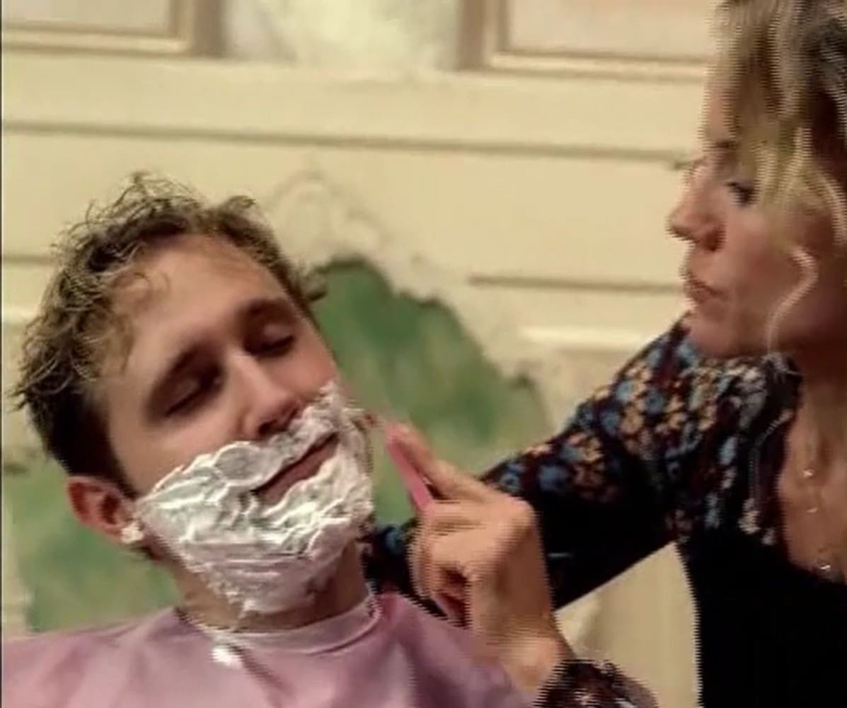 A woman shaving another man 's face with razor.